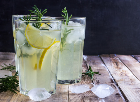 Cold lemon drink with rosemary, ice and tonic, on rustic wooden table. Selective focusの写真素材