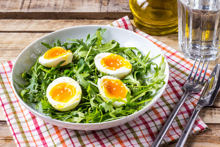 Spring salad with fresh vegetables: arugula, egg, and sesame on wooden background. Selective focusの写真素材