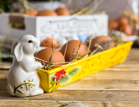 Porcelain Easter white bunny with colorful eggs on wooden background, selective focus