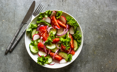 Salad with fresh spring vegetables on white plate and metal background. Top viewの写真素材