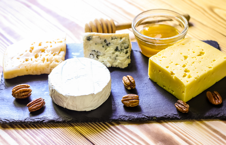 Cheese plate served with nuts and honey on a black slate board on a wooden backgroundの写真素材