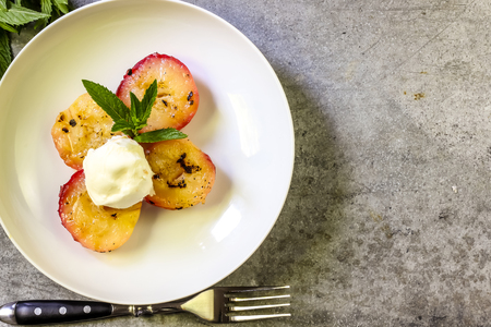 Baked peaches with ice cream on a plate on a gray metal backgroundの写真素材