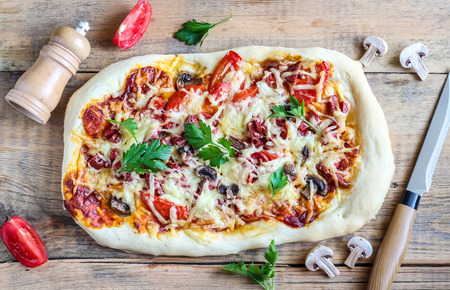 Tasty Italian pizza with pepperoni, tomatoes, cheese and mushrooms on a vintage wooden table.の写真素材