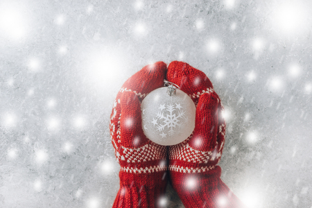Christmas balls decoration in female hands in knitted red mittens on lightの写真素材