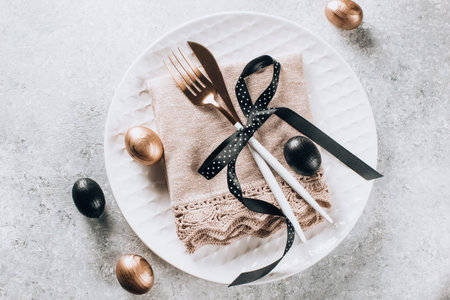 Easter table setting with black and bronze-colored decorative wooden eggs. Top view