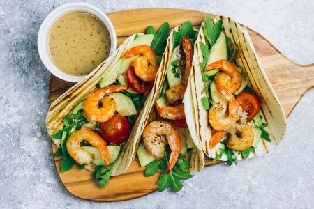 Seafood. Mexican food. Tortilla tacos with arugula, lemon, avocado and grilled shrimp pawns. On a light gray background. Top view copy spaceの写真素材