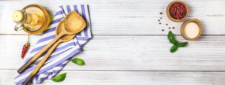 Cooking wooden utensils, olive oil, spices and light blue, white napkin on white wooden