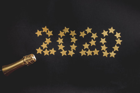 Bottle of champagne with gold confetti on black background. Top view, flat lay. Christmas...