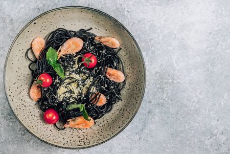 Black pasta with seafood. Traditional Italian cuisine - pasta with shrimp, tomato and basil in a ceramic plate on a rustic background. Flat lay, top view.の写真素材