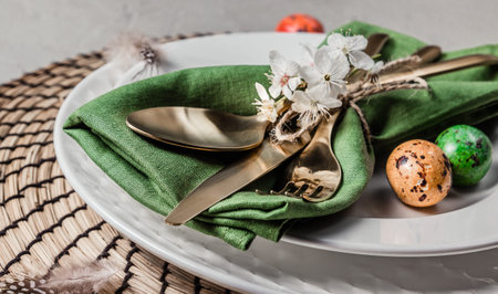 Easter table setting. Empty plates with green linen napkin and golden cutlery on concrete
