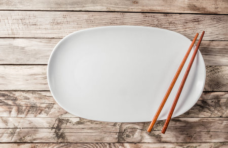 Vintage Table setting with oval plate and chopsticks on old rustic wooden table. Top view. Copy...