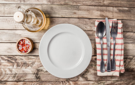 Vintage Table setting with obottle of oil, salt, napkin, fork, knife and plate on old rustic wooden...