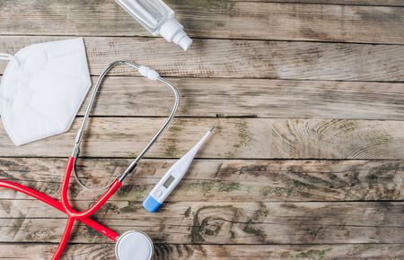 Red stethoscope, mask, thermometer and sanitizer on rustic woodenの写真素材