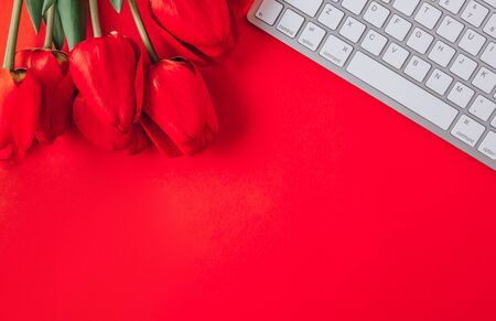 Home office workplace keyboard and tulip flowers on red background. Flat lay, top view, copy spaceの写真素材