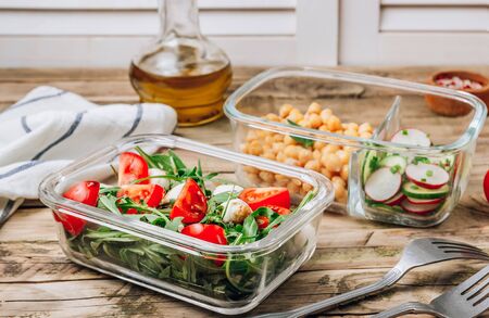 Healthy meal prep containers with chickpeas and spring salad with cucumbers, radish and chives and containers with caprese salad with arugula. Healthy lunch in glass containers. Zero waste concept.の写真素材