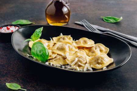 Tasty ravioli with parmesan and basil leaves on a black plate on a dark background. Italian food. Selective focusの写真素材