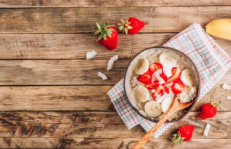 Quinoa porridge with coconut milk and fresh strawberries in a coconut bowl wooden rustic background. Healthy Lactose and Gluten Free Breakfast. Top view with copy spaceの写真素材