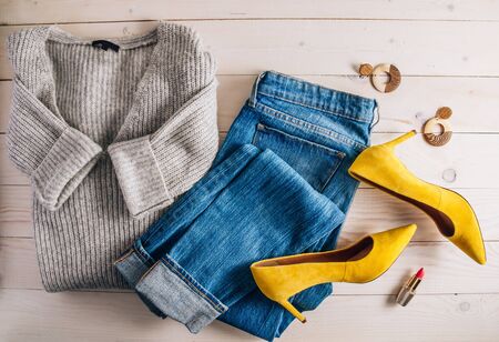 Female autumn and winter clothes flat lay on wooden background. Gray sweater, jeans and yellow shoes. Top viewの写真素材