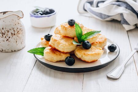 Trandy homemade food - fluffy mini pancakes with blueberries and mint on a white wooden background. Selective focus. Back lightの写真素材