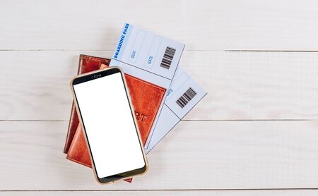 Boarding pass in in passport, toy airplane, and smartphone with blank screen on white wooden background. Top view. Flat layの写真素材