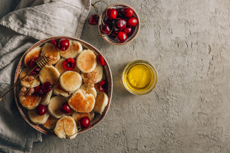 Trendy home breakfast with tiny pancakes in a bowl with honey and cherries on a concrete table. Top...