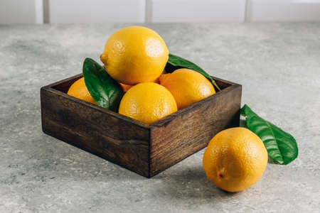 Fresh lemons in an old box with leaves on light gray backgroundの写真素材