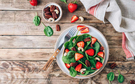 Fresh strawberry salad with spinach leaves and nuts on rustic wooden background. Healthy summer food. top view with copy spaceの写真素材