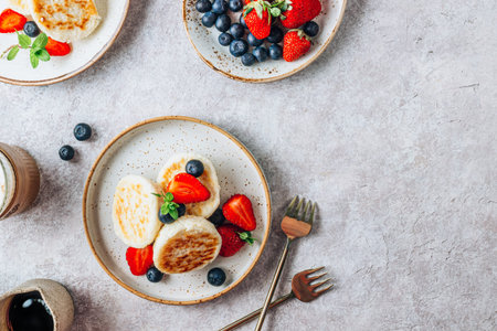 Cottage cheese pancakes, syrniki with fresh berries on light stone background. Low carb healthy...