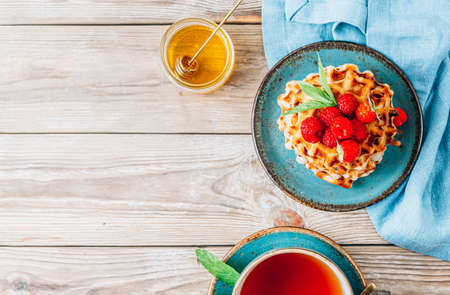 Stack of belgian waffles with honey, mint and fresh raspberries on turqouise plateの写真素材