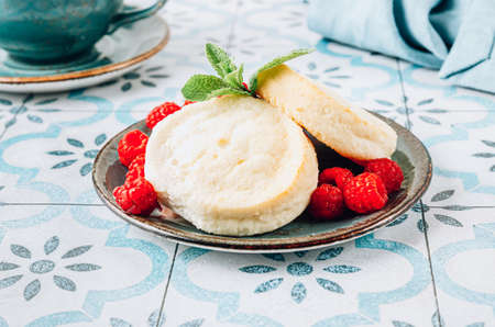 Mini cheesecakes with fresh raspberry on blue plate over tiled background. Syrniki, cottage cheese pancakesの写真素材