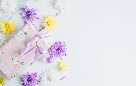 Flowers composition with white, purple and yellow chrysanthemum flowers and gift box on white marble...