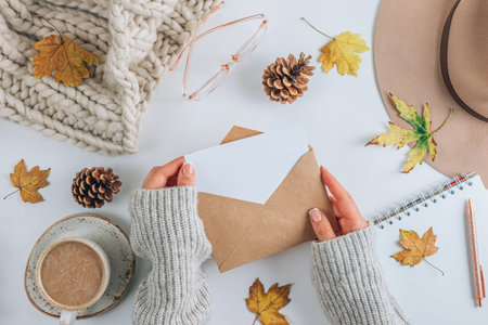 White and beige Autumn flat lay composition. Cup of coffee, scarf, glasses, cones, envelope and...