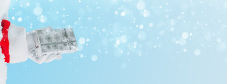 Santa Claus gloved hands holding giftbox. against light blue bokeh background. Holiday greeting card with copy space.の写真素材