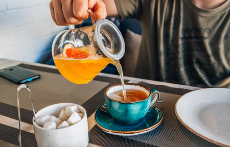 Close up of mans hand pouring fruit tea from glass kettle to cup. Cafe concept.の写真素材