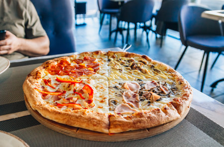 Italian pizza four seasons on a wooden board on a table in a cafe or restaurant. Man with a smartphone in his hand in the backgroundの写真素材