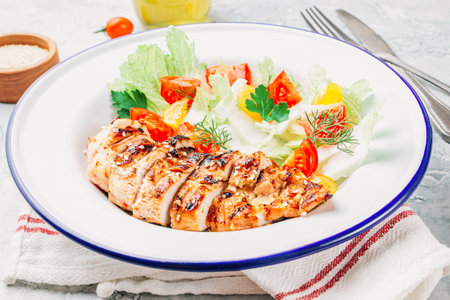 Fried chicken fillet and fresh vegetable salad of tomatoes over gray marble table. Grilled chicken breast. Healthy food.の写真素材