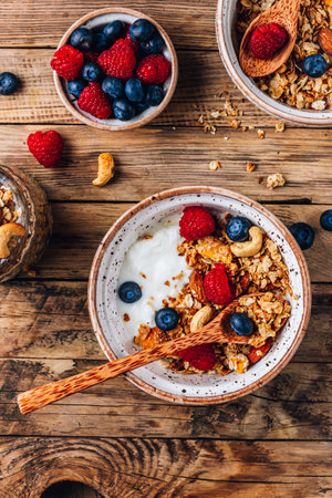 Healthy brakfast with yogurt and baked granola with berries in two small bowls, Granola baked with nuts, coconut oil and honey.の写真素材