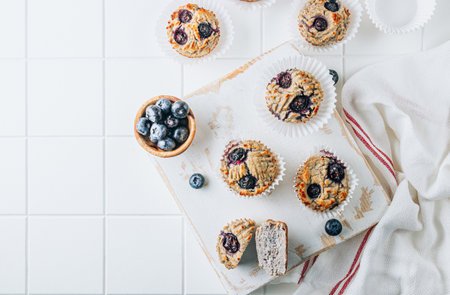 Healthy coconut muffins with blueberries. Only four ingredients , coconut flour, eggs, banana and blueberries on white tiled background.の写真素材