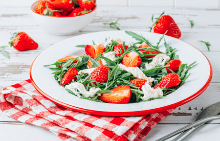 Fresh summer strawberry salad with arugula and stracciatella on white plate over rustic wooden backgroundの写真素材