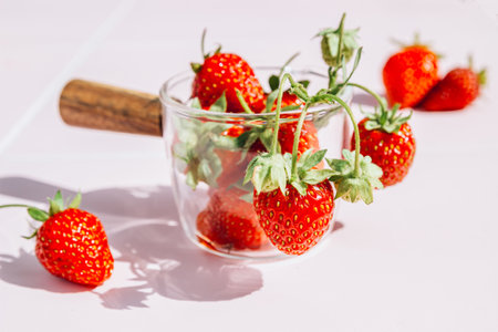 Burst of Freshness: Ripe Strawberries in a Glass Bowl on Pink Background with Hard Shadowsの写真素材