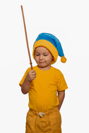 A cute little boy in yellow clothes holds a magic wand in his hand. On the head is a blue cap. Isolatedの写真素材