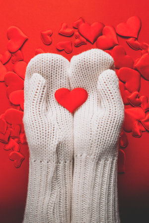 Hands in white knitted gloves hold red hearts on a colored backgroundの写真素材