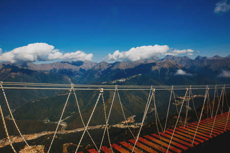 Suspension bridge in the mountains against the background of blue sky and beautiful cloudsの写真素材