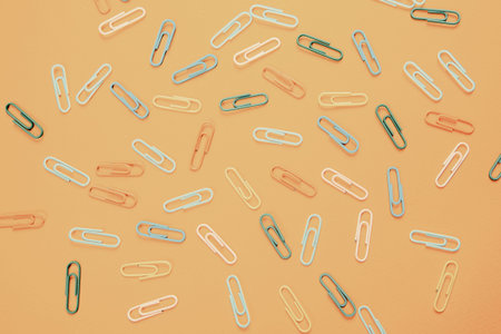 A lot of colorful paper clips lie on an orange background.
