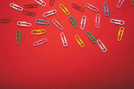 A lot of colorful paper clips lie on an red background.の写真素材