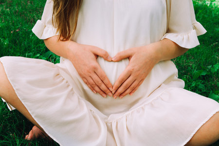 A pregnant woman in a white dress strokes, hugs, holds her hands on her stomach, against the...
