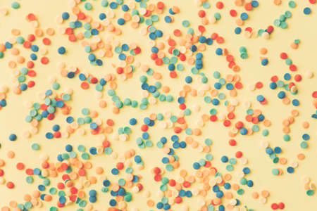 Colorful round candies are neatly scattered on a yellow background. Flat lay, top viewの写真素材
