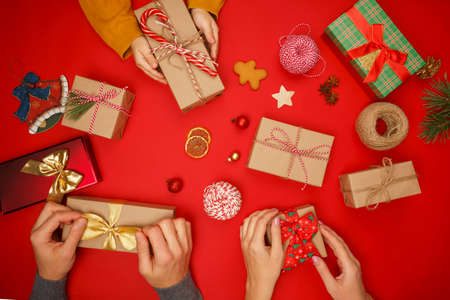 A family of three, mom, dad and child, pack Christmas gifts in craft paper and tie beautiful bows with their own handsの写真素材