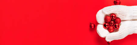 Red Christmas tree toys balls lie in female hands in white mittens. Winter Christmas banner with copy space.の写真素材