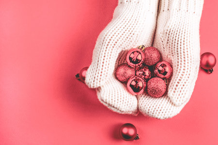 Pink Christmas tree toys balls lie in female hands in white mittens. Winter Christmas background with copy space.の写真素材
